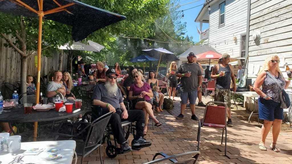 A group of people enjoying drinks at an outdoor patio with umbrellas on a sunny day.