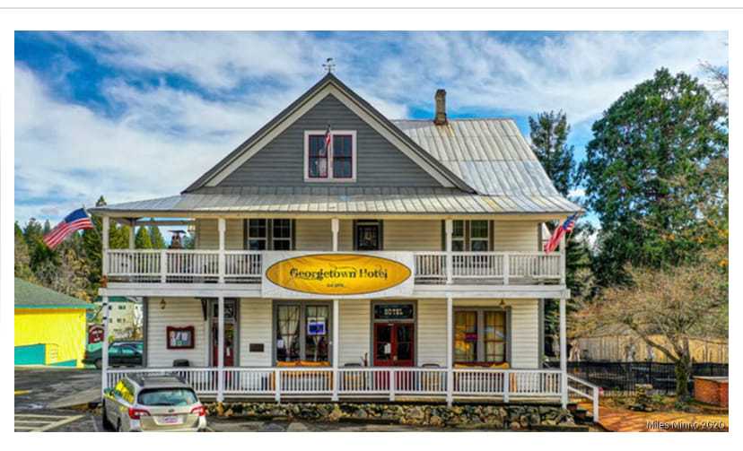 Two-story Georgetown hotel with flags, balcony, and a rustic charm on a sunny day.